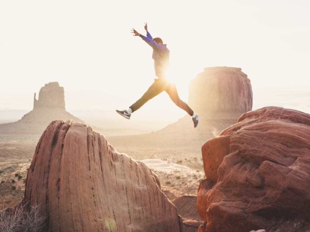 man jumping over two rocks with sun behind him