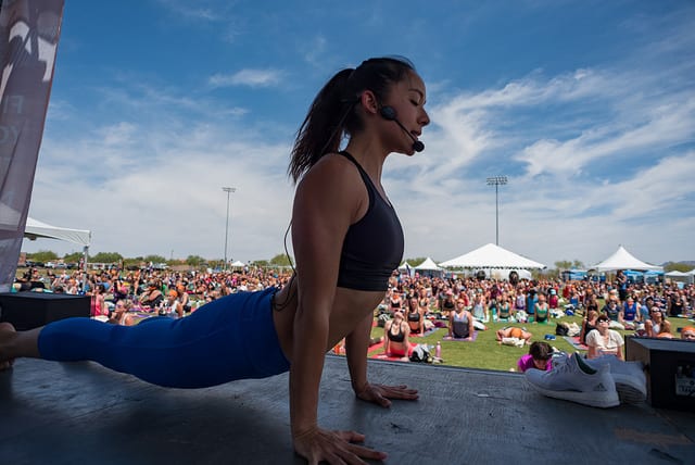 woman on stage teaching yoga to field of people