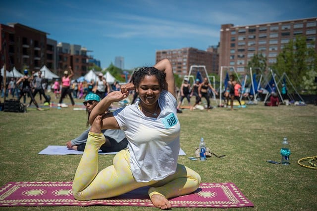 woman in field doing king pigeon pose with aerial rigs in background in atlanta