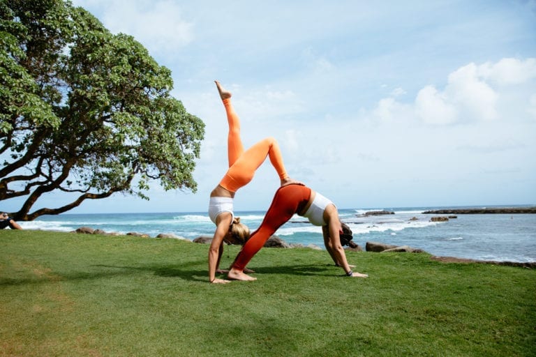 Two women in a partner pose on the grass by the ocean.