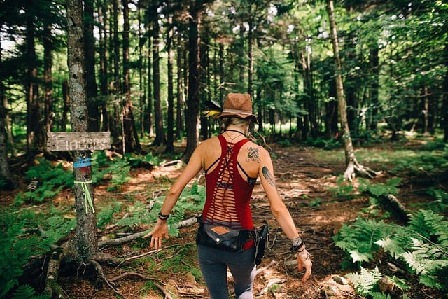 woman walking into woods on hike wearing hat