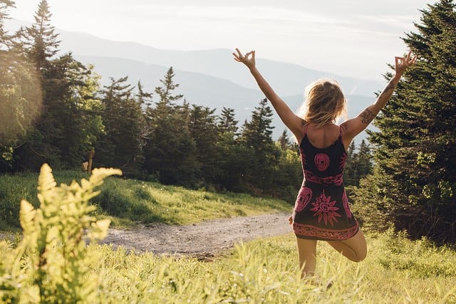 woman in tree pose in woods overlooking mountain