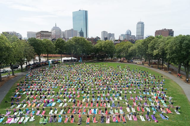 people in large crowd doing yoga with boston skyline behind them