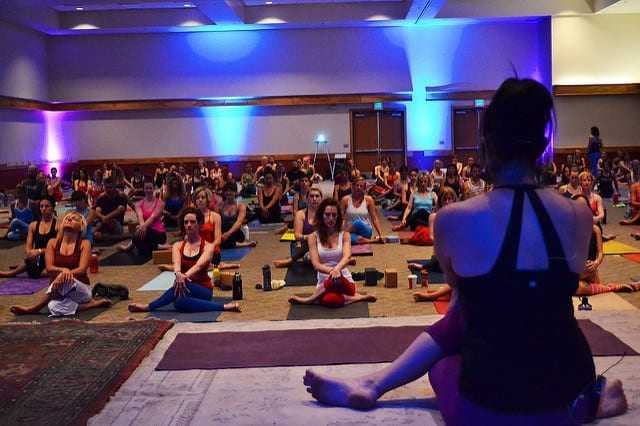 woman teaching yoga from stage in cow pose