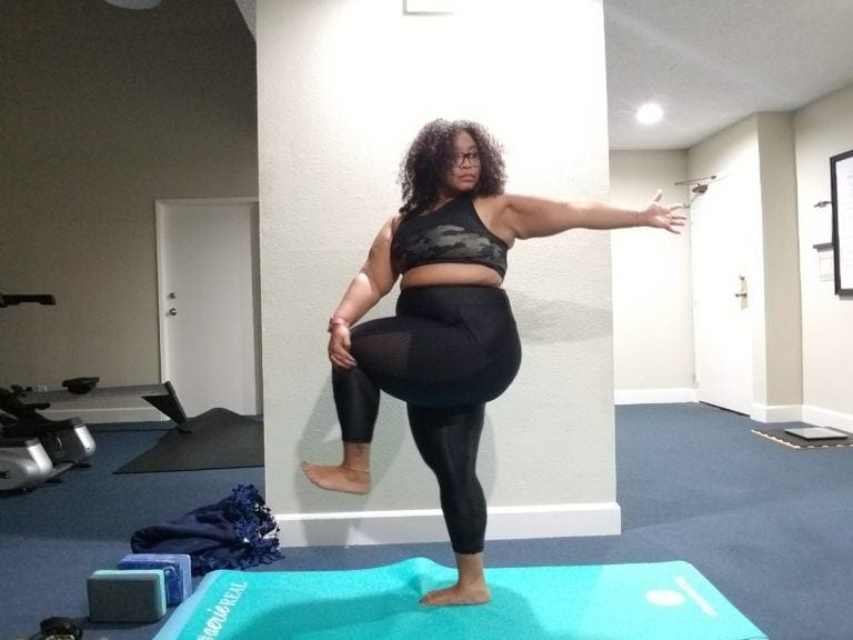 woman in tree pose against wall on turquoise yoga mat