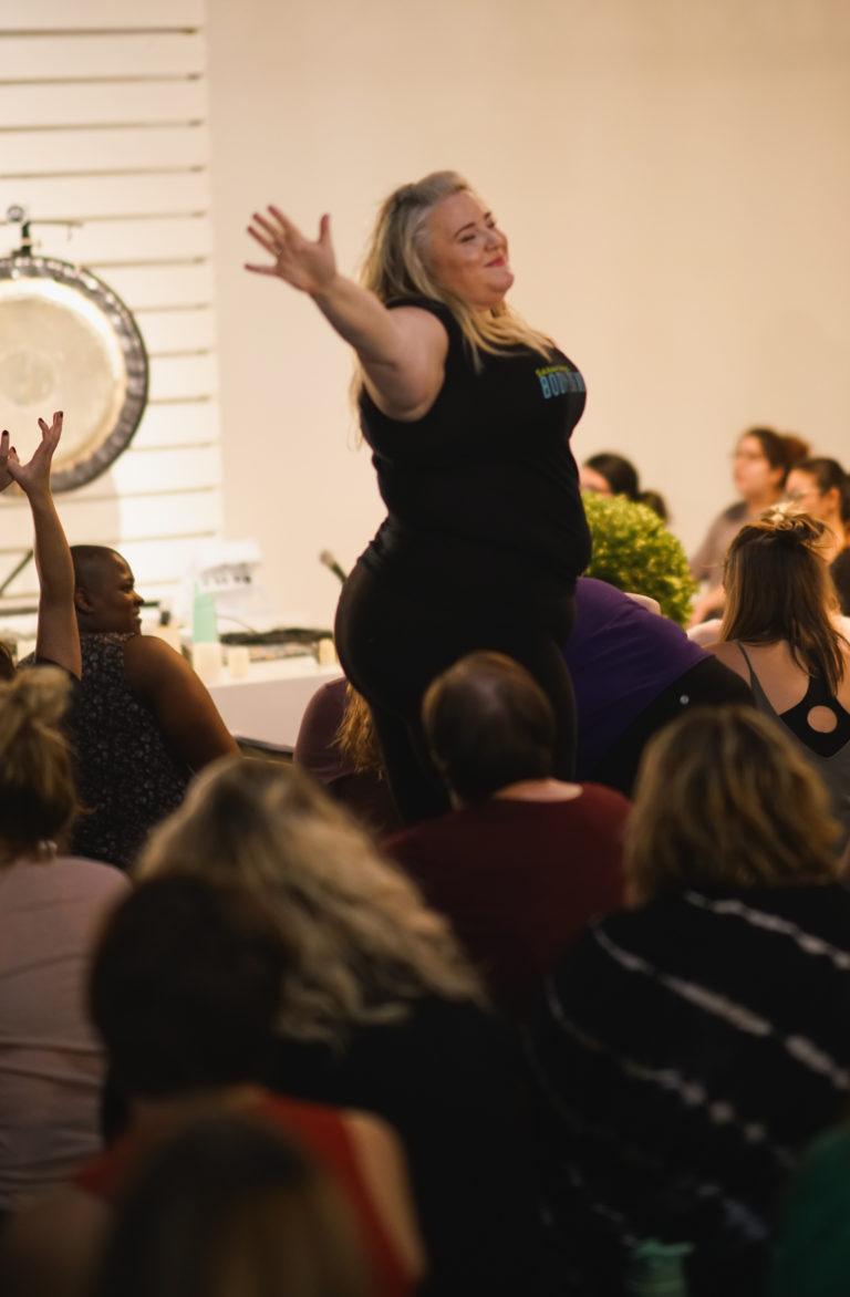 woman standing with arms raised in workshop with gong