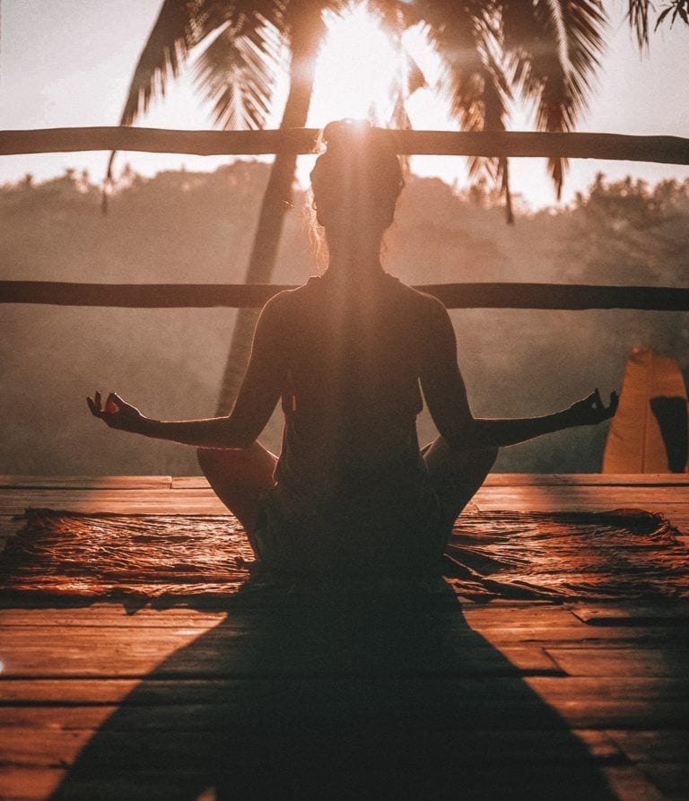 woman sitting meditating on porch with palm trees