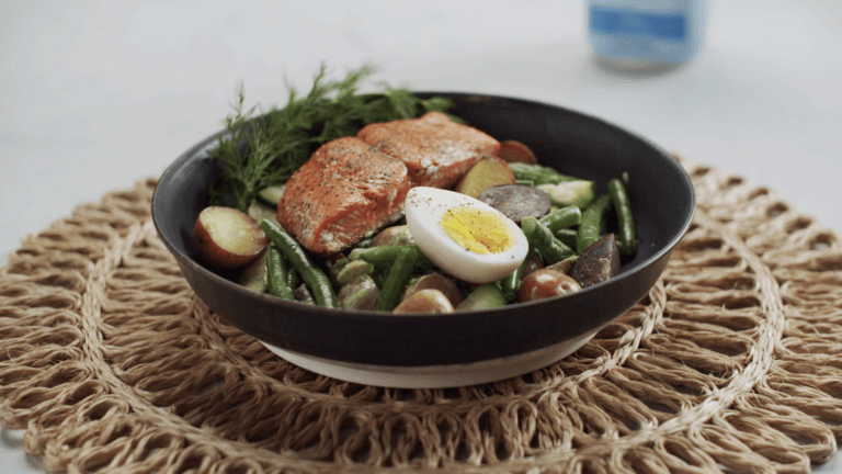 bowl with salmon, egg, and green beans on a table.