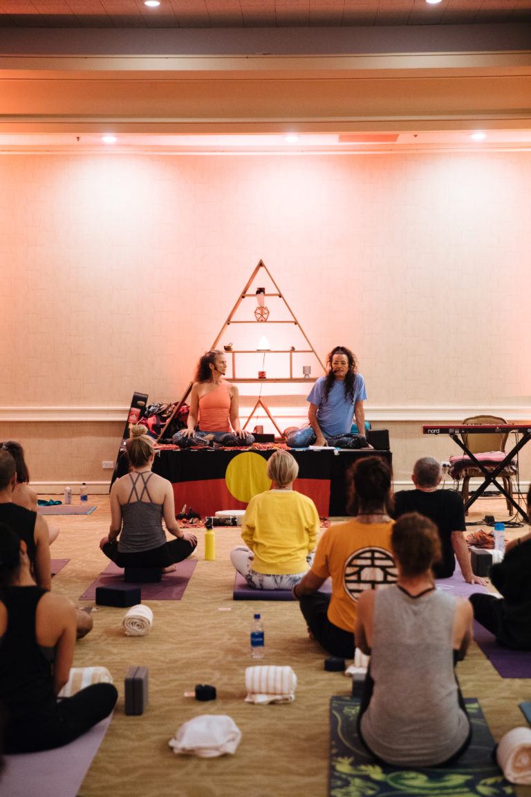 yoga teachers on stage teaching with triangle altar behind them 